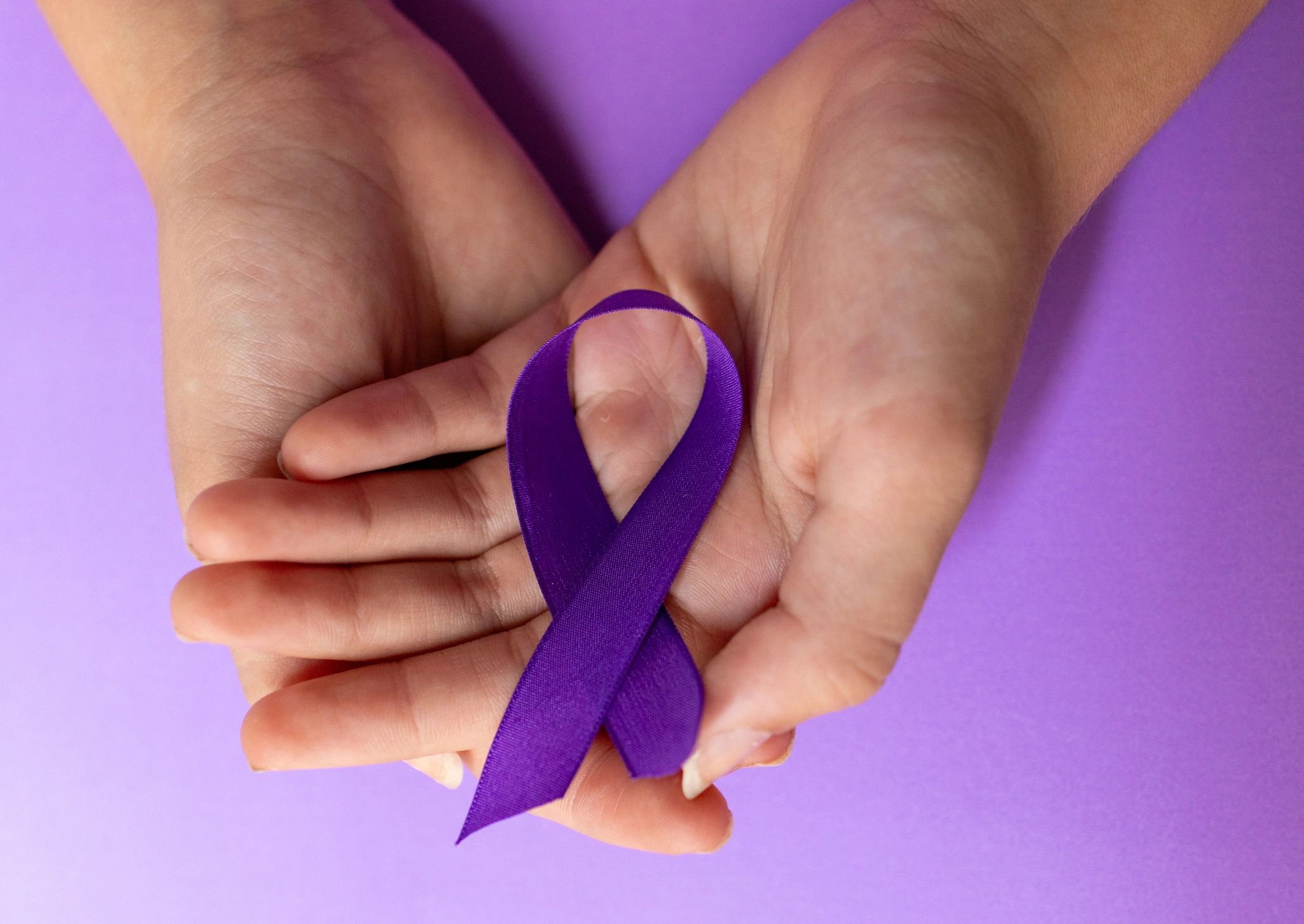 Two hands holding a purple awareness ribbon